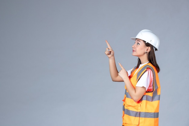 Vista frontal del constructor femenino en uniforme en la pared blanca