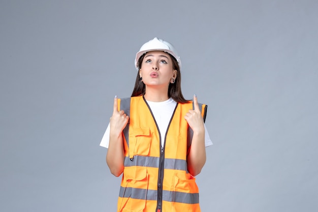 Vista frontal del constructor femenino en uniforme en la pared gris