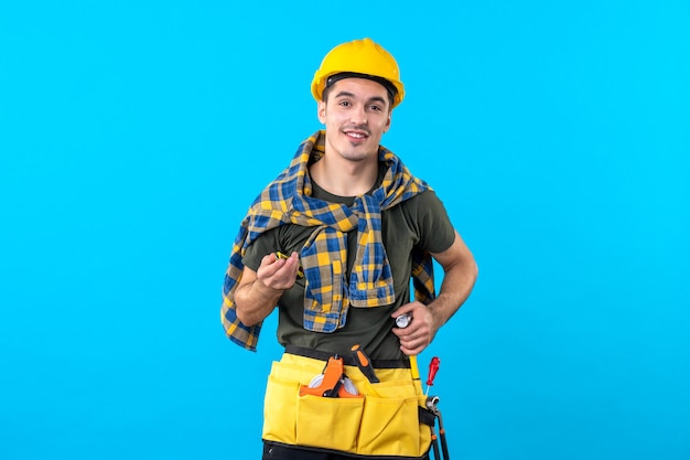 Vista frontal constructor masculino en casco con diferentes herramientas en el fondo azul trabajo de construcción constructor de arquitectura plana constructor trabajador de la casa