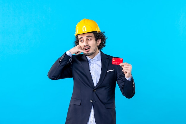 Vista frontal del constructor masculino sosteniendo una tarjeta bancaria sobre fondo azul trabajo arquitectura empresarial trabajo edificio ingeniero de color