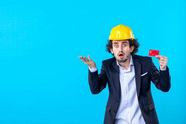Vista frontal del constructor masculino en traje sosteniendo una tarjeta bancaria roja sobre fondo azul trabajo arquitectura empresarial trabajo ingeniero constructor color del edificio