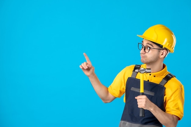 Vista frontal del constructor masculino en uniforme con un martillo en sus manos sobre la pared azul