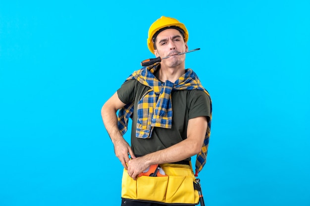 vista frontal construtor masculino com capacete segurando uma chave de fenda com a boca no fundo azul arquitetura plana construção civil construtores trabalhadores