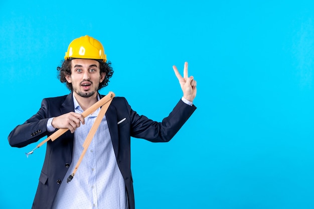 vista frontal construtor masculino no capacete segurando uma figura geométrica de madeira no fundo azul arquitetura trabalho construtor emprego design empresarial