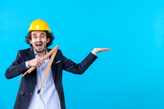 vista frontal construtor masculino no capacete segurando uma figura geométrica de madeira no fundo azul arquitetura trabalho trabalho projeto empresarial construtor edifício