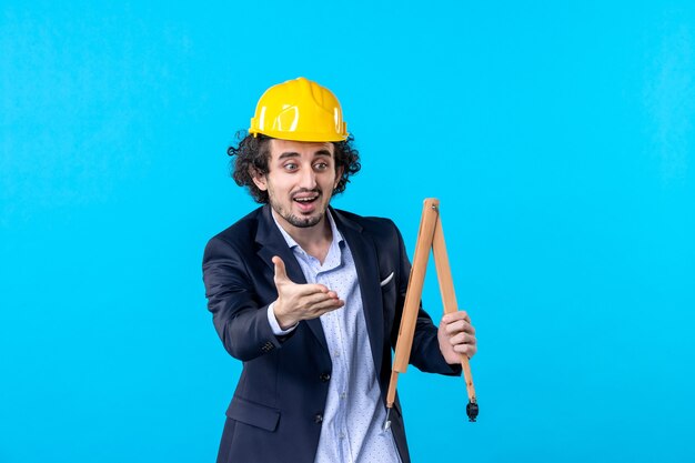 vista frontal construtor masculino segurando um dispositivo de madeira no fundo azul trabalho design de negócios construtor arquitetura trabalho de construção