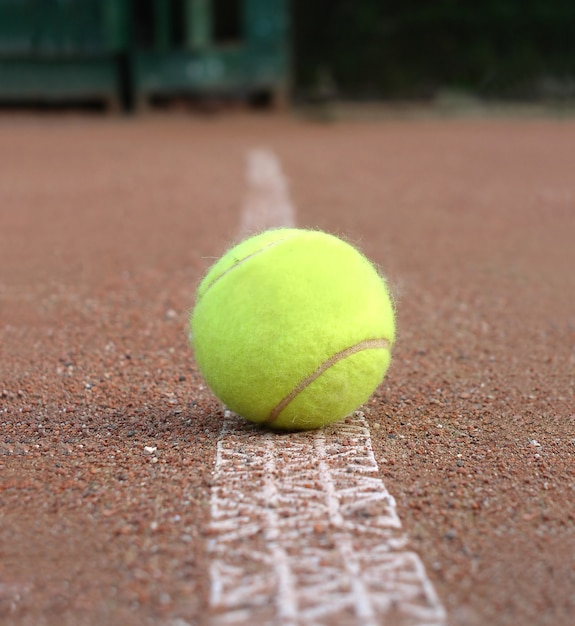 Vista frontal da bola de tênis amarela ao ar livre na quadra de solo marcando a linha de perto