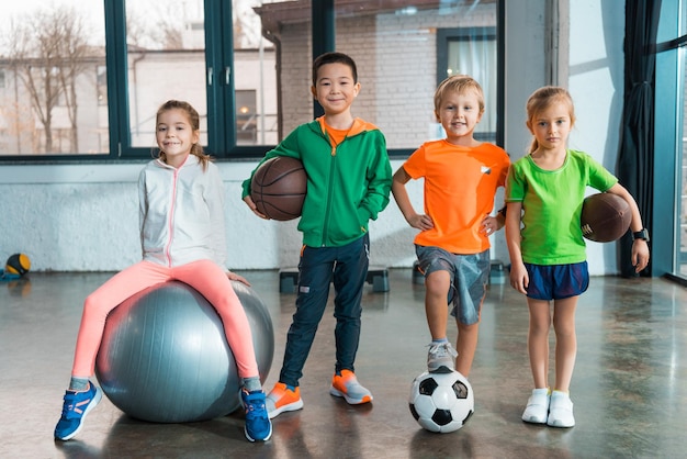 Vista frontal da criança sentada na bola de fitness ao lado de crianças multiétnicas com bolas no ginásio