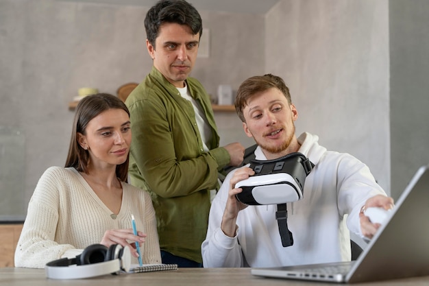 Vista frontal da equipe de pessoas usando laptop e fone de ouvido de realidade virtual