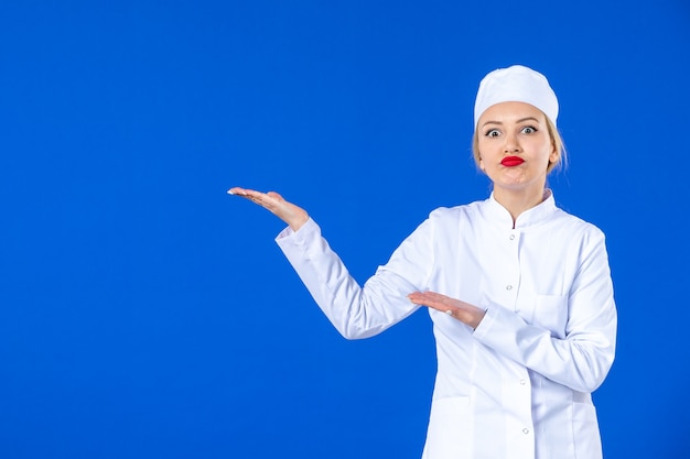 vista frontal da jovem enfermeira em traje médico na parede azul