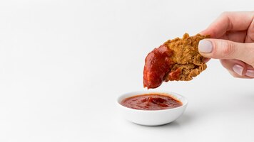 Vista frontal da mão mergulhando frango frito no ketchup com cópia-espaço