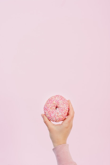 Foto vista frontal da mão segurando rosquinha vitrificada com granulado e copie o espaço