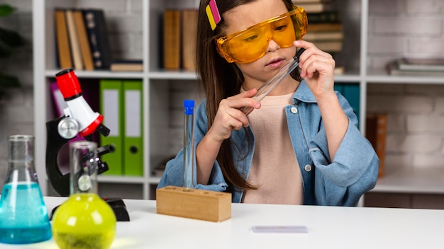 Foto vista frontal da menina com óculos de segurança e microscópio