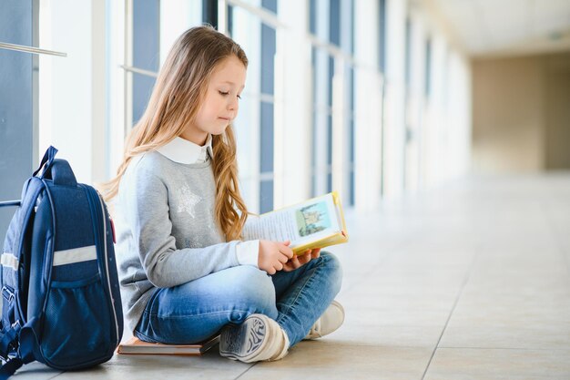 Vista frontal da menina da escola loira bonita segurando muitas notas coloridas e livros Menina adolescente inteligente sorrindo para a câmera em pé no corredor da escola internacional