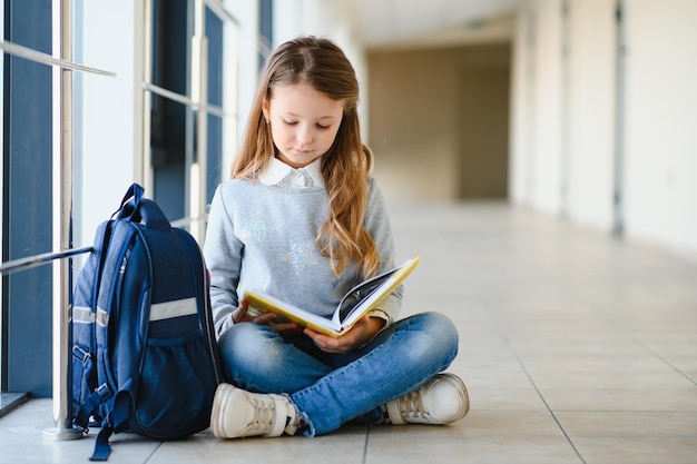 Vista frontal da menina linda escola entre corredor na escola segurando notas nas mãos Menina engraçada e feliz sorrindo para a câmera descansando depois das aulas na escola primária