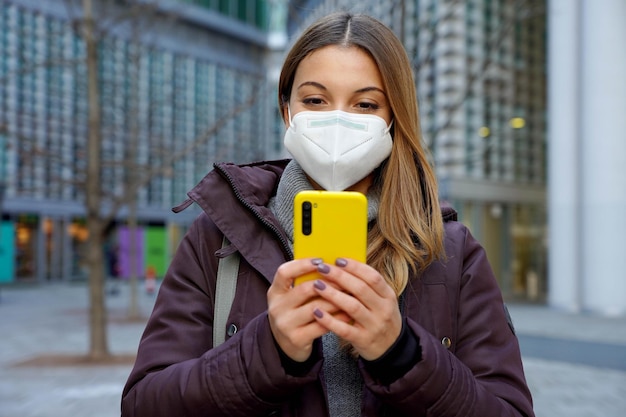 Vista frontal da mulher de inverno com máscara protetora ffp2 kn95 conversando com smartphone na rua da cidade