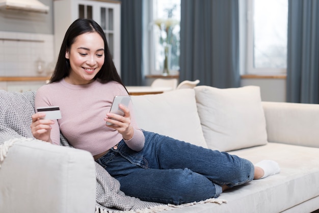 Vista frontal da mulher no sofá, fazer pedidos on-line usando cartão de crédito e smartphone