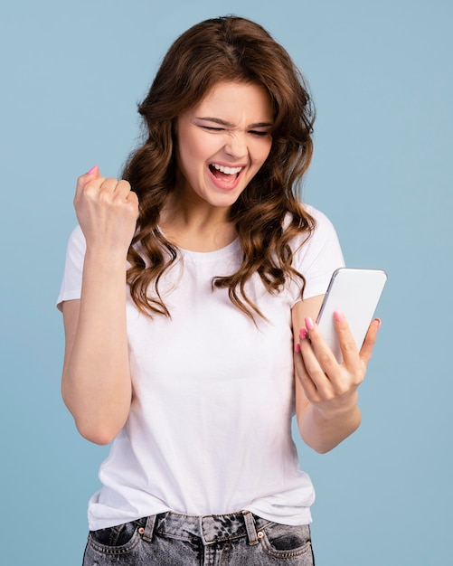 Vista frontal da mulher sendo vitoriosa segurando um smartphone