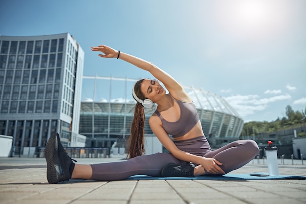 Vista frontal de una dama complacida haciendo una flexión lateral sentada con el brazo levantado