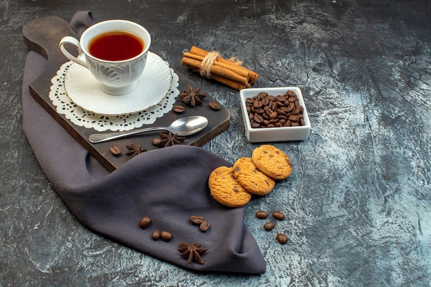 Vista frontal de biscoitos caseiros, limão, canela e uma xícara de chá na tábua de madeira, grãos de café no fundo de gelo