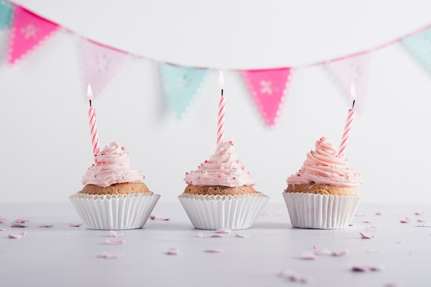 Vista frontal de cupcakes de aniversário com velas acesas e guirlandas