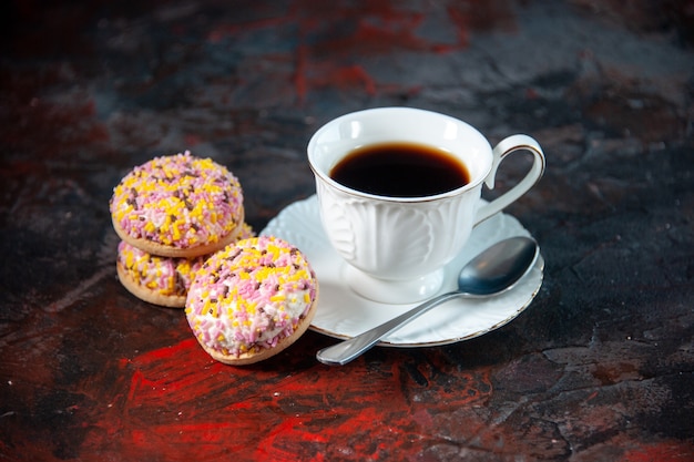 Vista frontal de deliciosos biscoitos de açúcar caseiros e uma xícara de café no fundo escuro de cores misturadas com espaço livre