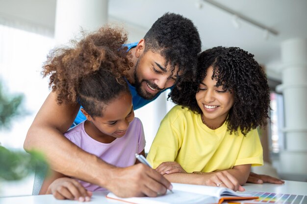 Vista frontal de pais afro-americanos ajudando sua filha com lição de casa na mesa