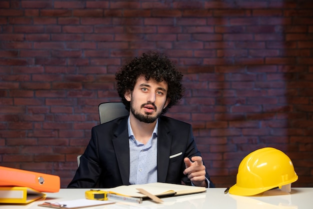 vista frontal de um engenheiro sentado atrás do local de trabalho em um terno de empreiteiro de negócios de negócios de construtor corporativo agenda de trabalho