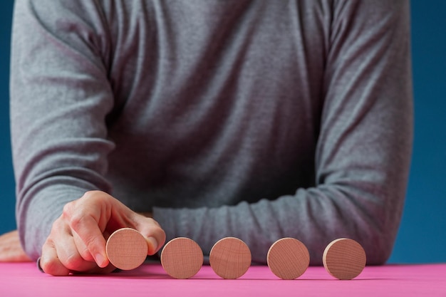 Vista frontal de um homem colocando cinco círculos de corte de madeira em branco seguidos na superfície rosa na frente dele