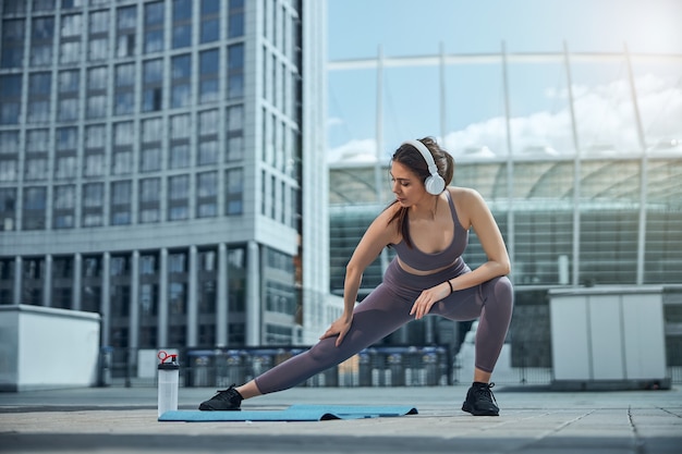 Vista frontal de um jovem atleta de top e legging fazendo uma estocada lateral