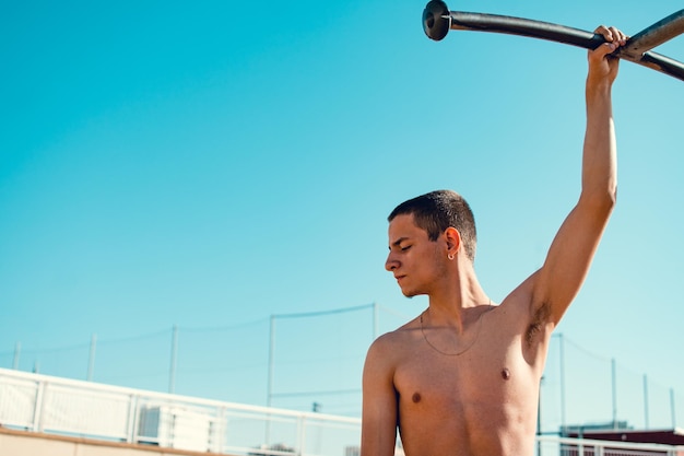 Vista frontal de um jovem garoto caucasiano segurando seu braço em uma barra de ginástica
