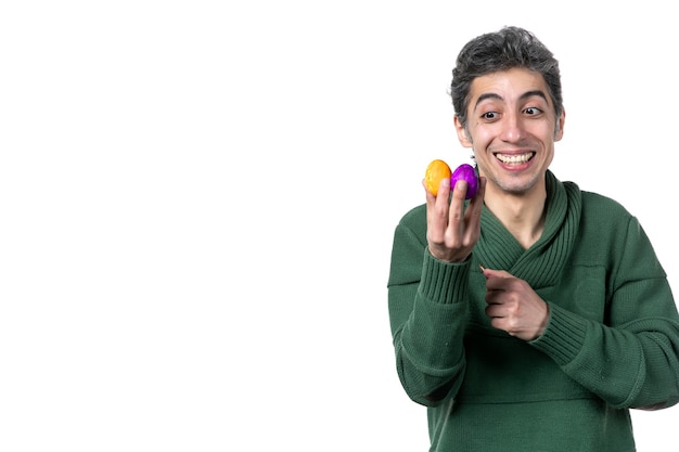 vista frontal de um jovem segurando ovos pintados de cores na parede branca