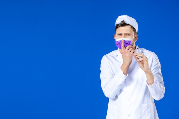 Vista frontal de um médico em traje médico e máscara roxa segurando injeção em azul