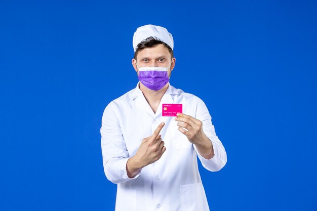 Vista frontal de um médico em traje médico e máscara segurando um cartão de crédito em azul