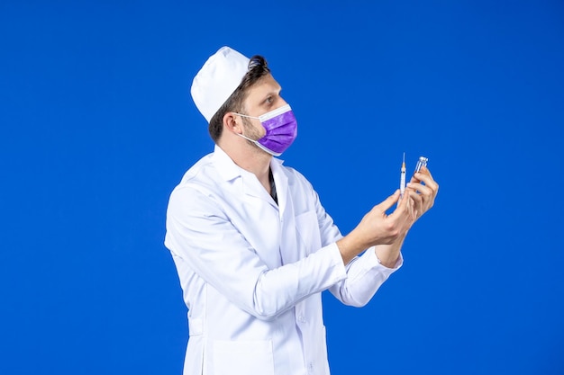 Vista frontal de um médico em traje médico e máscara segurando vacina e injeção em azul