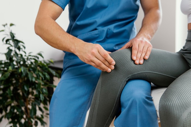 Foto vista frontal de um terapeuta osteopático masculino verificando o joelho de uma paciente