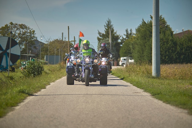 Vista frontal de um triciclo na estrada que chega ao local de tiro, acompanhado por uma equipe de motociclistas.