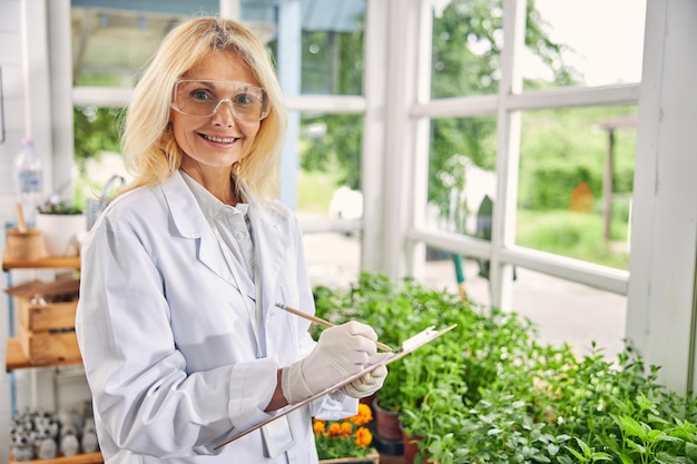 Vista frontal de uma bióloga sorridente e atraente usando óculos de proteção e luvas descartáveis de látex