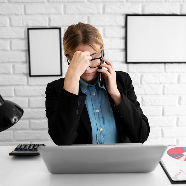 Foto vista frontal de uma empresária no escritório parecendo irritada enquanto fala ao telefone