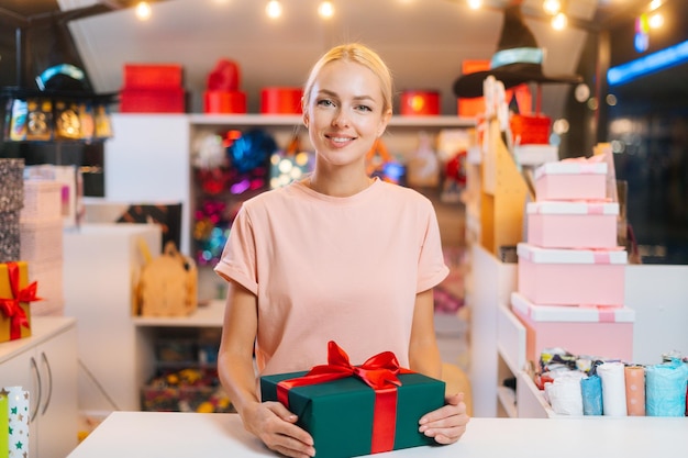 Foto vista frontal de uma jovem feliz segurando uma caixa de presente de natal, amarrando uma fita vermelha e decorando