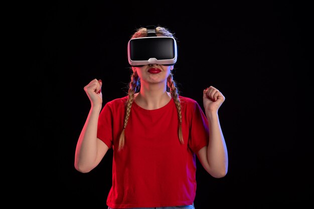 Vista frontal de uma jovem mulher jogando vr na parede escura