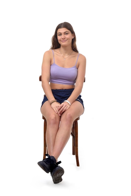 Vista frontal de uma jovem sentada na cadeira com pernas esticadas no fundo branco