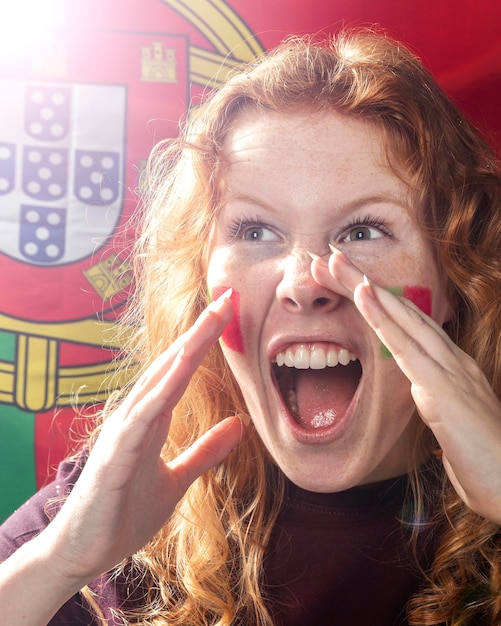 Foto vista frontal de uma mulher a aplaudir com a bandeira de portugal no rosto