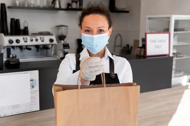 Foto vista frontal de uma mulher com máscara médica segurando um saco de papel com comida para viagem