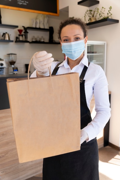 Foto vista frontal de uma mulher com máscara médica segurando um saco de papel com comida para viagem