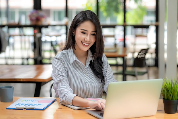Vista frontal de uma mulher de negócios asiática jovem atraente, sentada usando gráfico de laptop colocado no escritório.