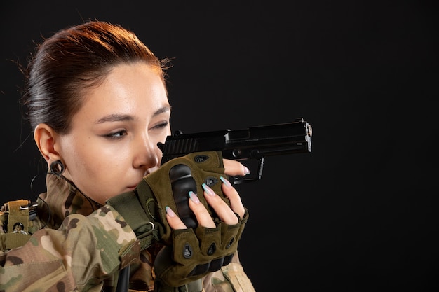 Foto vista frontal de uma mulher soldado com arma de uniforme na parede preta