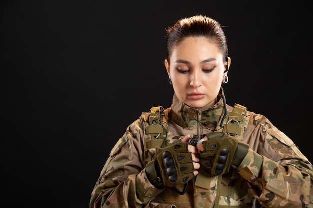 Vista frontal de uma mulher soldado com uma granada de uniforme na parede preta