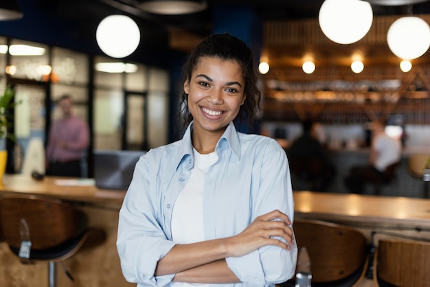 Foto vista frontal de uma mulher sorridente posando com os braços cruzados no local de trabalho