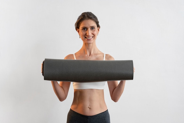 Vista frontal de uma mulher sorridente segurando um tapete de ioga